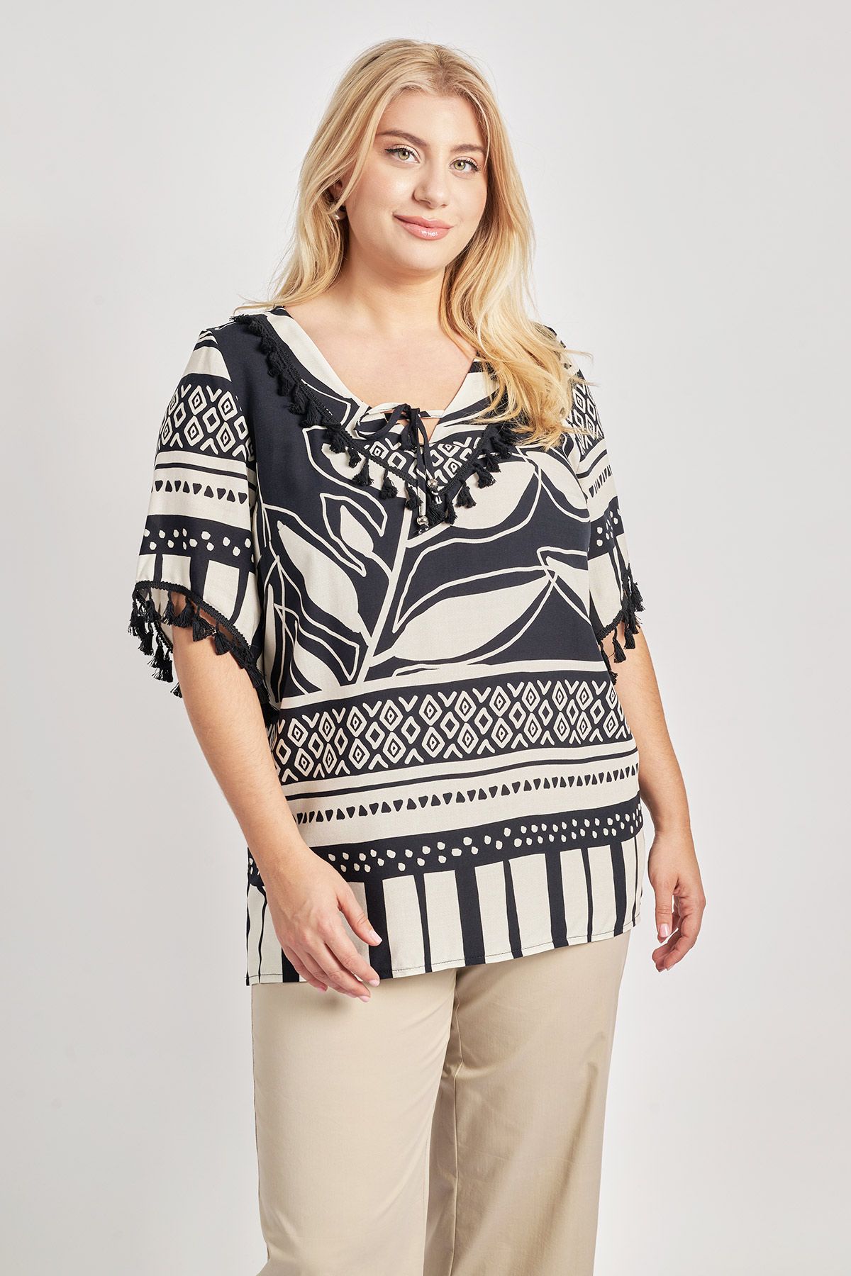 Μπλούζα από βισκόζη σε εμπριμέ με boho μοτίβο. V λαιμόκοψη με διακοσμητικά φουντάκια και δέσιμο. Κοντά μανίκια ασύμμετρα με φουντάκια. Σε ίσια γραμμή. Πλαϊνά ανοίγματα. Το μοντέλο έχει ύψος 177εκ, στήθος 110, μέση 85, περιφέρεια 115 και φοράει μέγεθος S