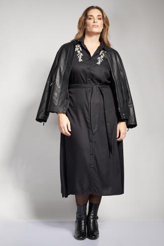 Αναδείξτε τη θηλυκότητά σας με αυτό το elegant μαύρο φόρεμα σε γραμμή πουκαμίσα από απαλής υφής ρεγιόν. Έννα κομμάτι που συνδυάζει την κλασική γοητεία με μοντέρνες λεπτομέρειες. Το σχέδιο ξεχωρίζει για τα λευκά κεντημένα λουλούδια στους ώμους, που προσδίδουν μια ρομαντική και φωτεινή νότα στο σκούρο φόντο. Διαθέτει γιακά, κλείσιμο με κουμπιά σε όλο το μήκος και ζώνη από το ίδιο ύφασμα που τονίζει τη μέση, προσφέροντας μια κολακευτική σιλουέτα. Τα μακριά μανίκια με το διακριτικό κλείσιμο στις μανσέτες και το midi μήκος του το καθιστούν ιδανικό για προσεγμένες εμφανίσεις από το πρωί στο γραφείο μέχρι μια βραδινή έξοδο. Συνδυάστε το με κλασικές μαύρες γόβες για ένα ολοκληρωμένο outfit διαχρονικής μόδας. Το μοντέλο έχει ύψος 180 εκ στήθος 107 μέση 95 περιφέρεια 122 και φοράει το μέγεθος S